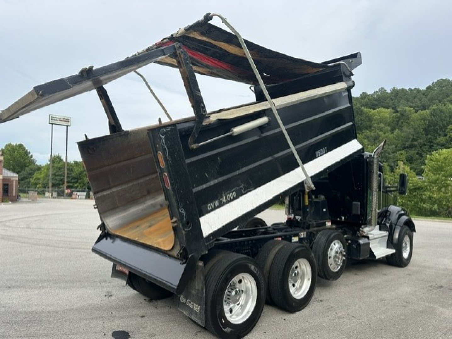 Kenworth T880 dump truck with empty bed raised on a hydraulic lift, side view showing multiple axles and tires.