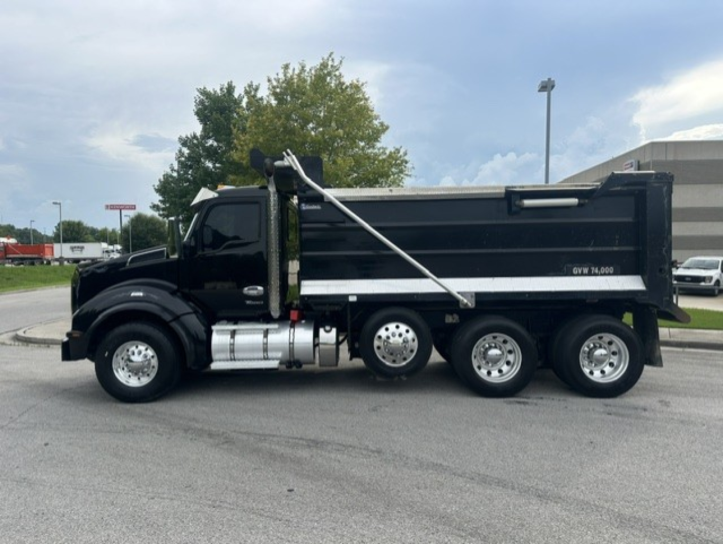 Kenworth T880 dump truck side view with black cab and dump bed, chrome fuel tanks, and dual rear axles.