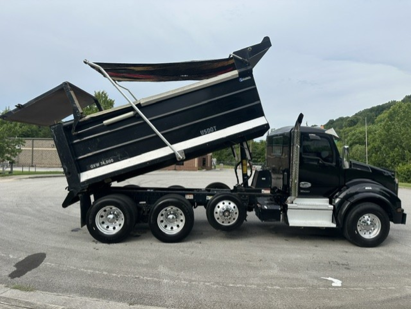 Kenworth T880 dump truck side view showing raised black dump bed and multiple axles; includes cab with black paint and chrome accents, wheel rims, and hydraulic lifting mechanism.