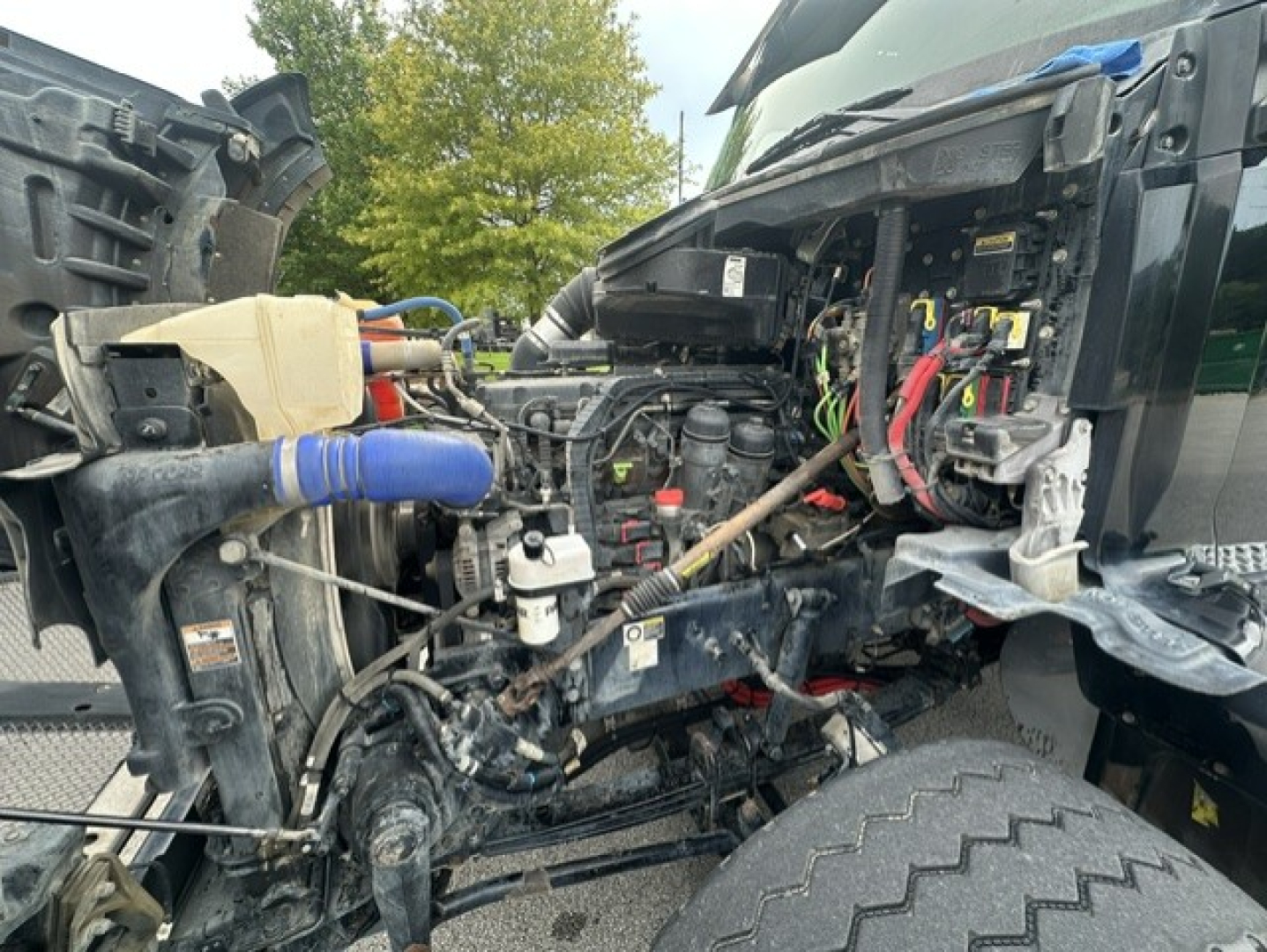 Kenworth T880 engine bay with exposed components and wiring; blue hose, coolant reservoir, and various hoses visible.