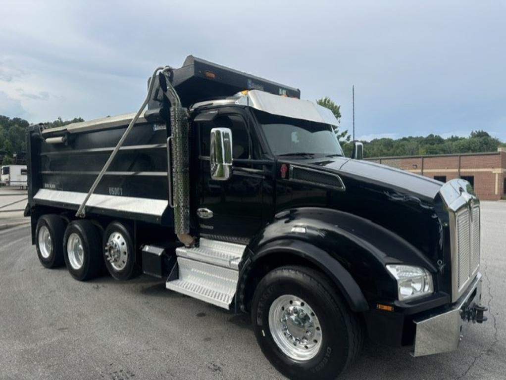 Kenworth T880 dump truck in service showing black cab and dump body with chrome accents and side steps.