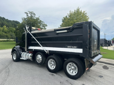 Kenworth T880 dump truck with black dump box and white reflective stripe, three rear axles, side view.