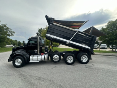 Kenworth T880 dump truck side view showing dump bed raised and rear wheels, with black cab and chrome fuel tanks.