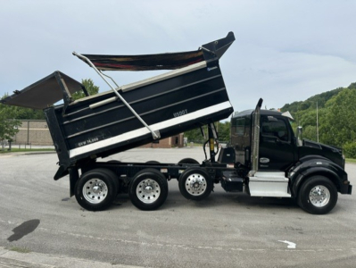 Kenworth T880 dump truck side view showing raised black dump bed and multiple axles; includes cab with black paint and chrome accents, wheel rims, and hydraulic lifting mechanism.