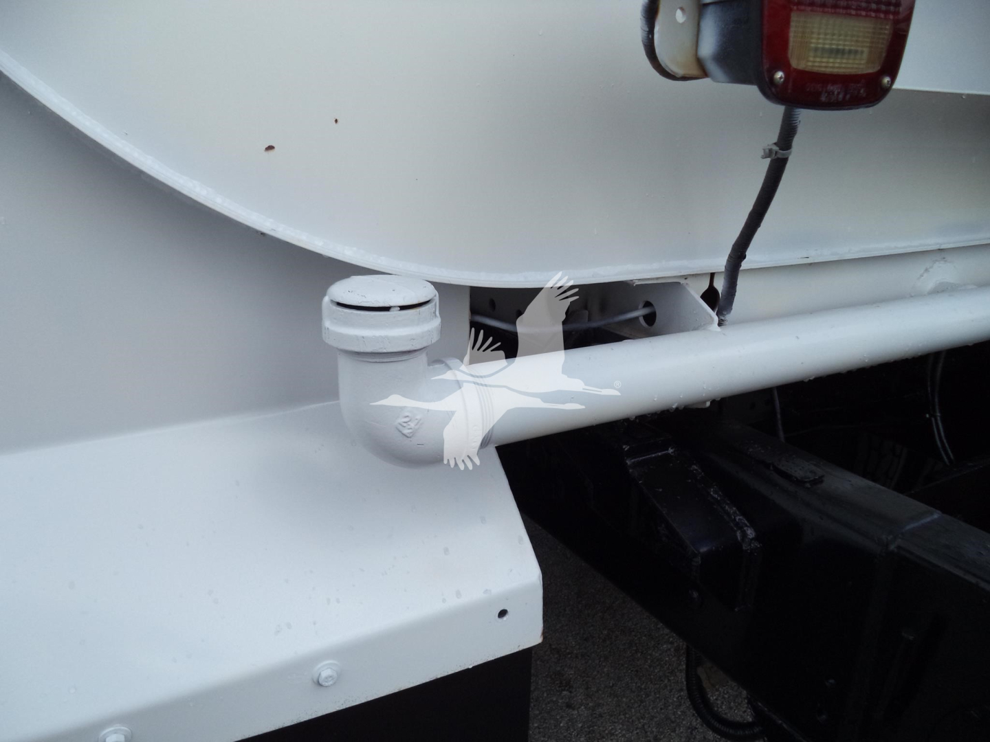 Rear left side of a Ford F650 truck showing a pintle hitch and taillight area with white paint and hitch linkage.