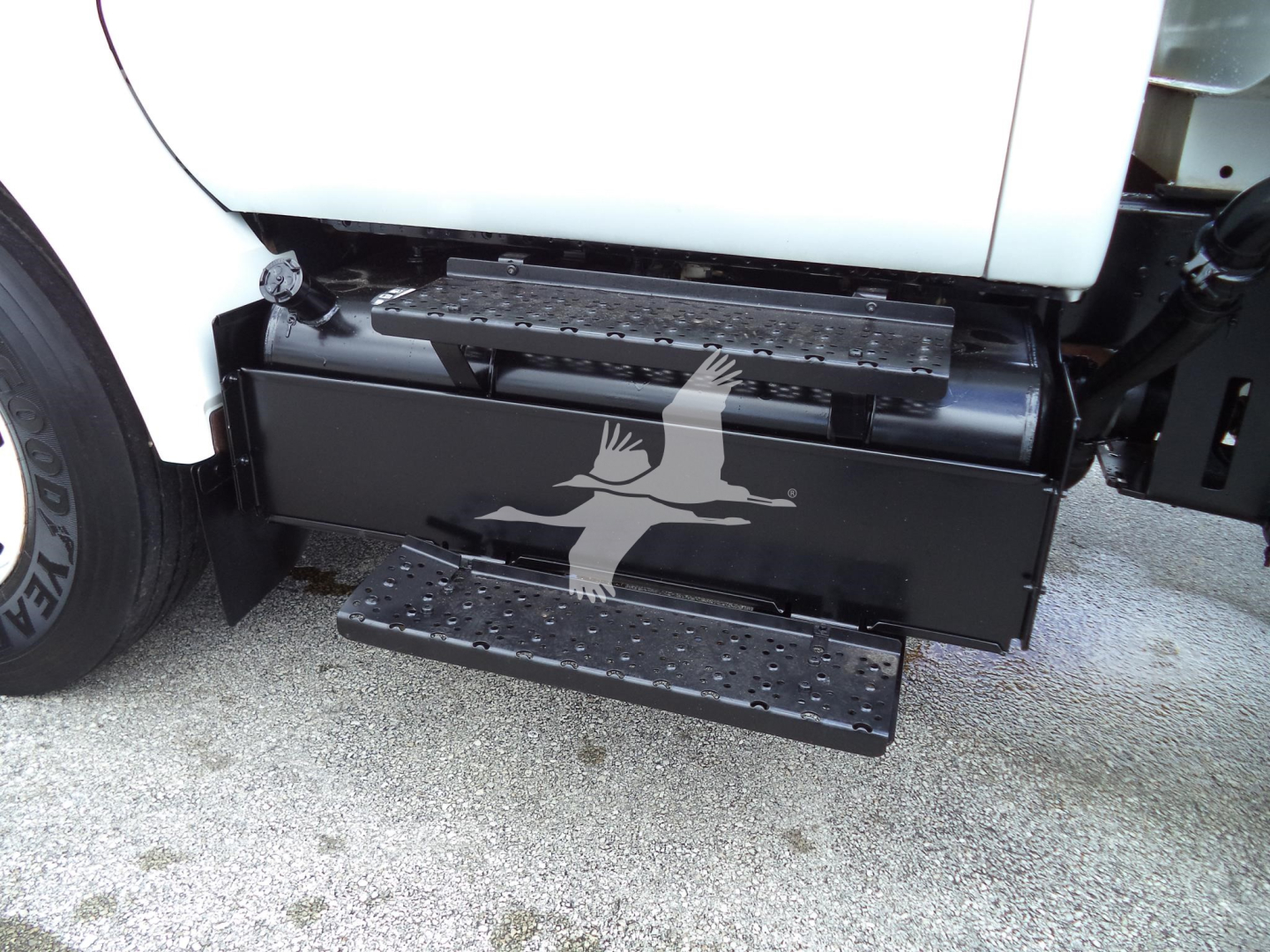 Truck side view showing a black fuel/auxiliary tank with steps under the cab of a 2017 Ford F650 SD truck, part of the chassis visible.