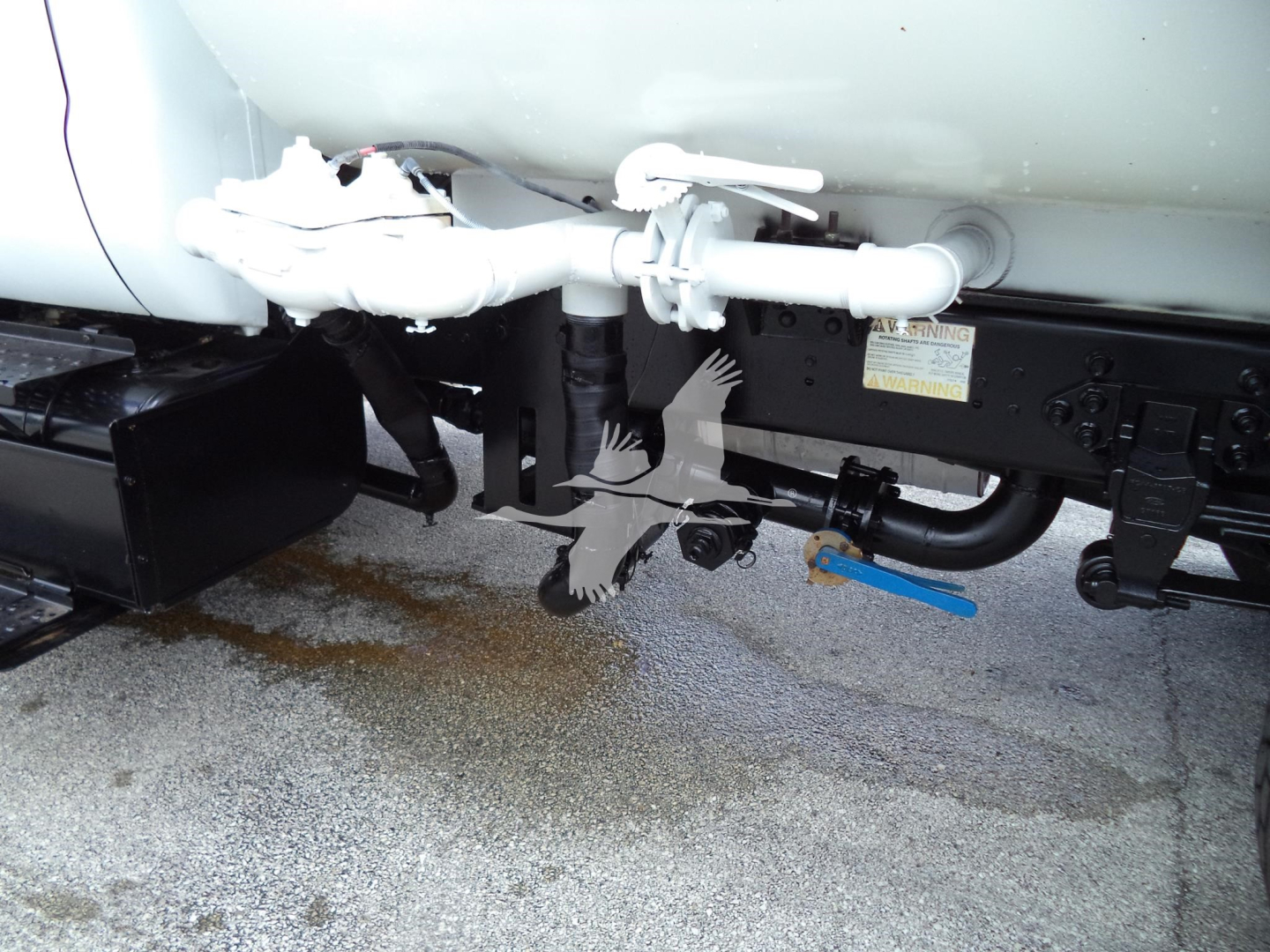 Underbody view of 2017 Ford F650 dual rear undercarriage showing piping, valve, and blue lever with label; part of water truck system.