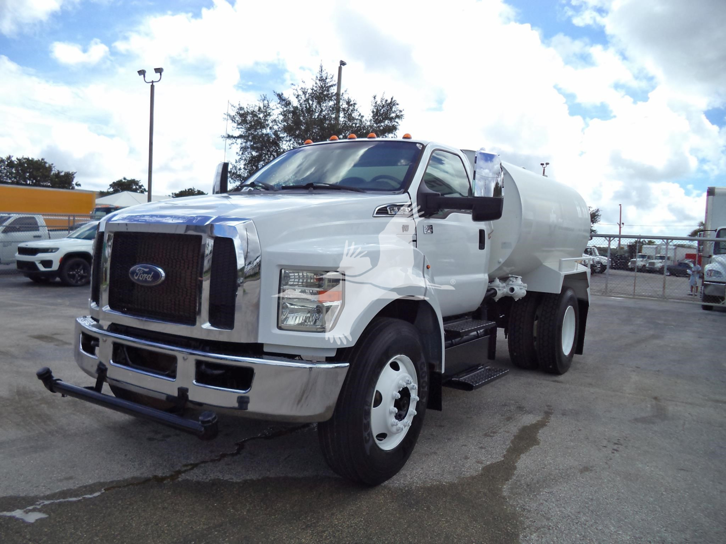 Ford F650 water tanker truck in a parking lot, white cab with tank behind; front bumper and grille visible.