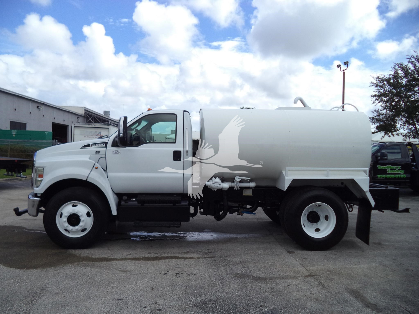 Ford F650 water truck side view showing tank and cab with white and gray livery.