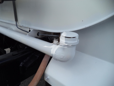 Ford F-650 fuel/auxiliary tank fittings showing pipe and capped valve with clamp and hoses in light gray paint.