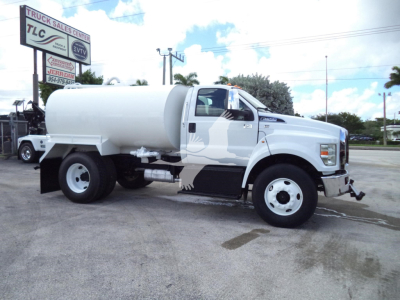 Ford F650 water truck in service condition with cylindrical tank mounted on chassis, side mirror, and front bumper.