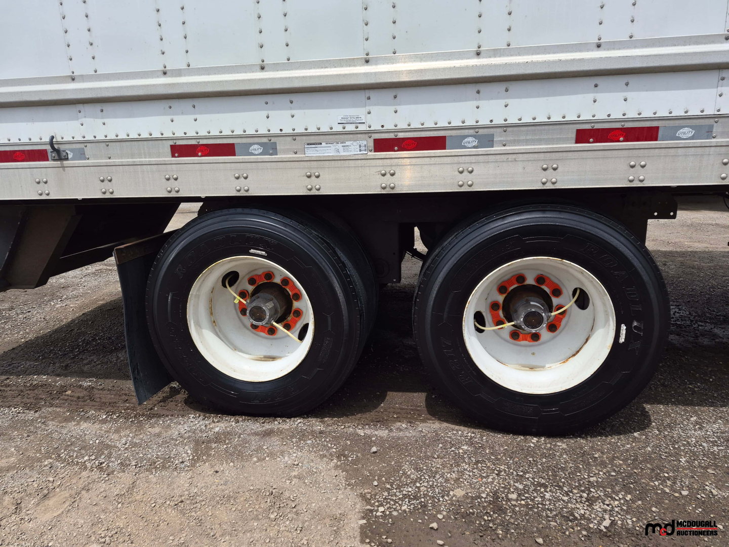 Dual rear axles of a 53' dry van trailer showing white wheels with orange lug nuts and black tires.