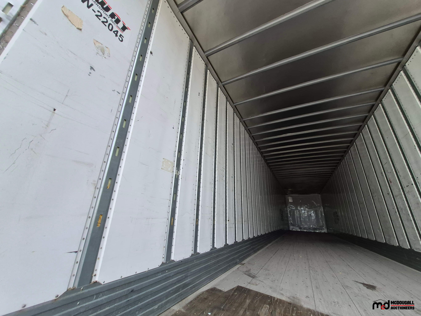 Inside view of a 53' dry van trailer cargo area with metal sidewalls and a wooden floor; partial VIN tag and numbers on left door.
