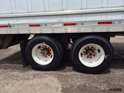 Dual rear axles of a 53' dry van trailer showing white wheels with orange lug nuts and black tires.