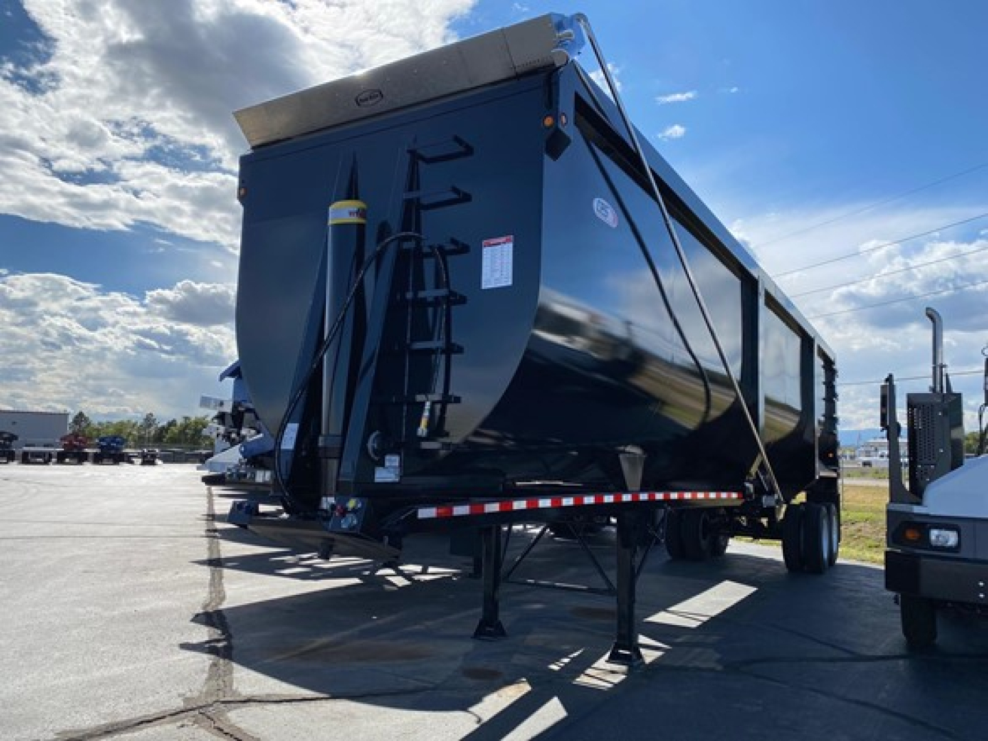 Dump trailer in a parking lot showing a CPS Ar450 gas/dump body with support legs, ladder, and hydraulic components visible.