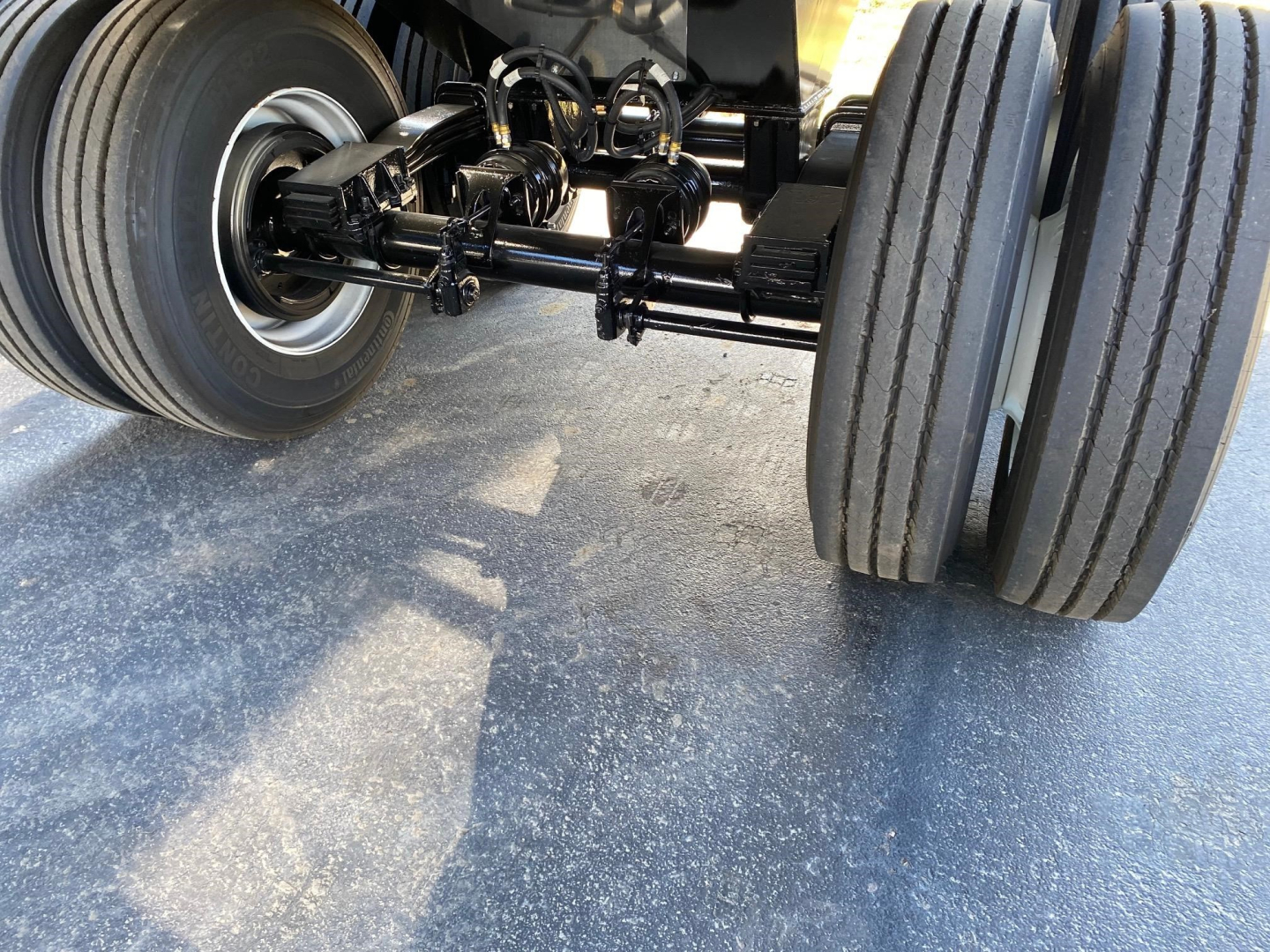 Trailer axle assembly with dual rear tires and suspension components visible, showing metal linkage and leaf springs under the trailer frame.