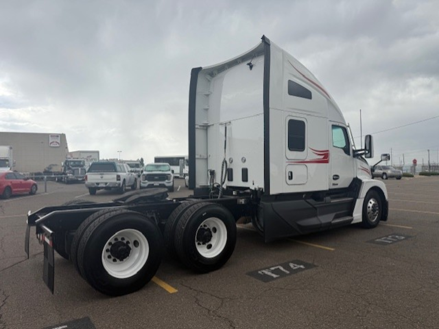 Kenworth T680 cab with sleeper in a parking lot, side view showing dual rear axles and white wheels