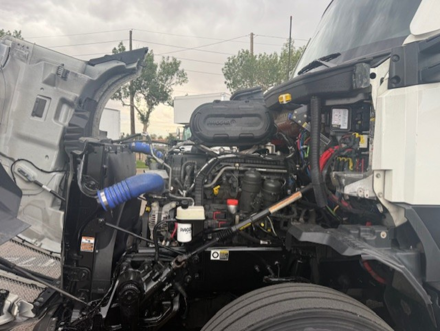 Kenworth T680 engine bay view with exposed components and wiring illustrating the engine and front wheel area.