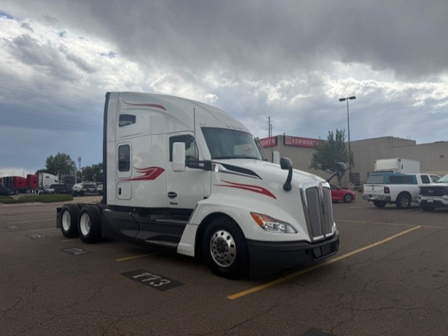 Kenworth T680 sleeper cab truck in a parking lot, side view with white paint and red decals.