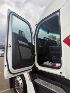 Kenworth T680 cab exterior with open driver door showing interior seating and steps.
