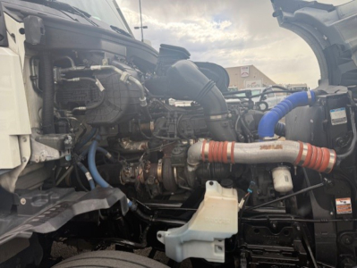 Kenworth T680 engine bay showing large turbocharger and blue and red hoses with coolant reservoir and various engine components.