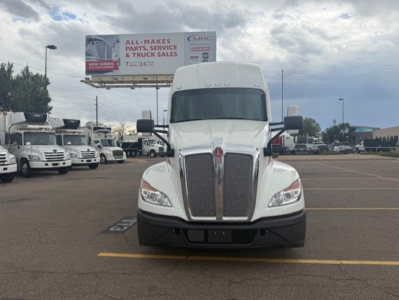 Kenworth T680 truck in a parking lot, front view, chrome grille, white cab, billboard in background.