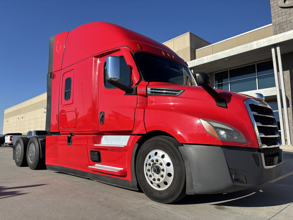 Red Freightliner PT126064ST truck cab in profile view showing front bumper, wheel, and sleeper cab.