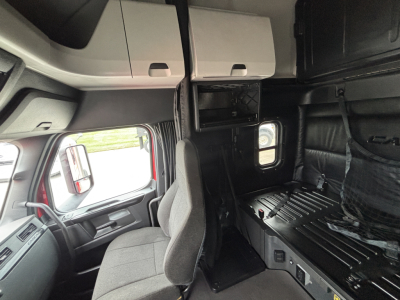 Cab interior of a Freightliner truck showing sleeper area and cockpit with overhead storage cabinets.