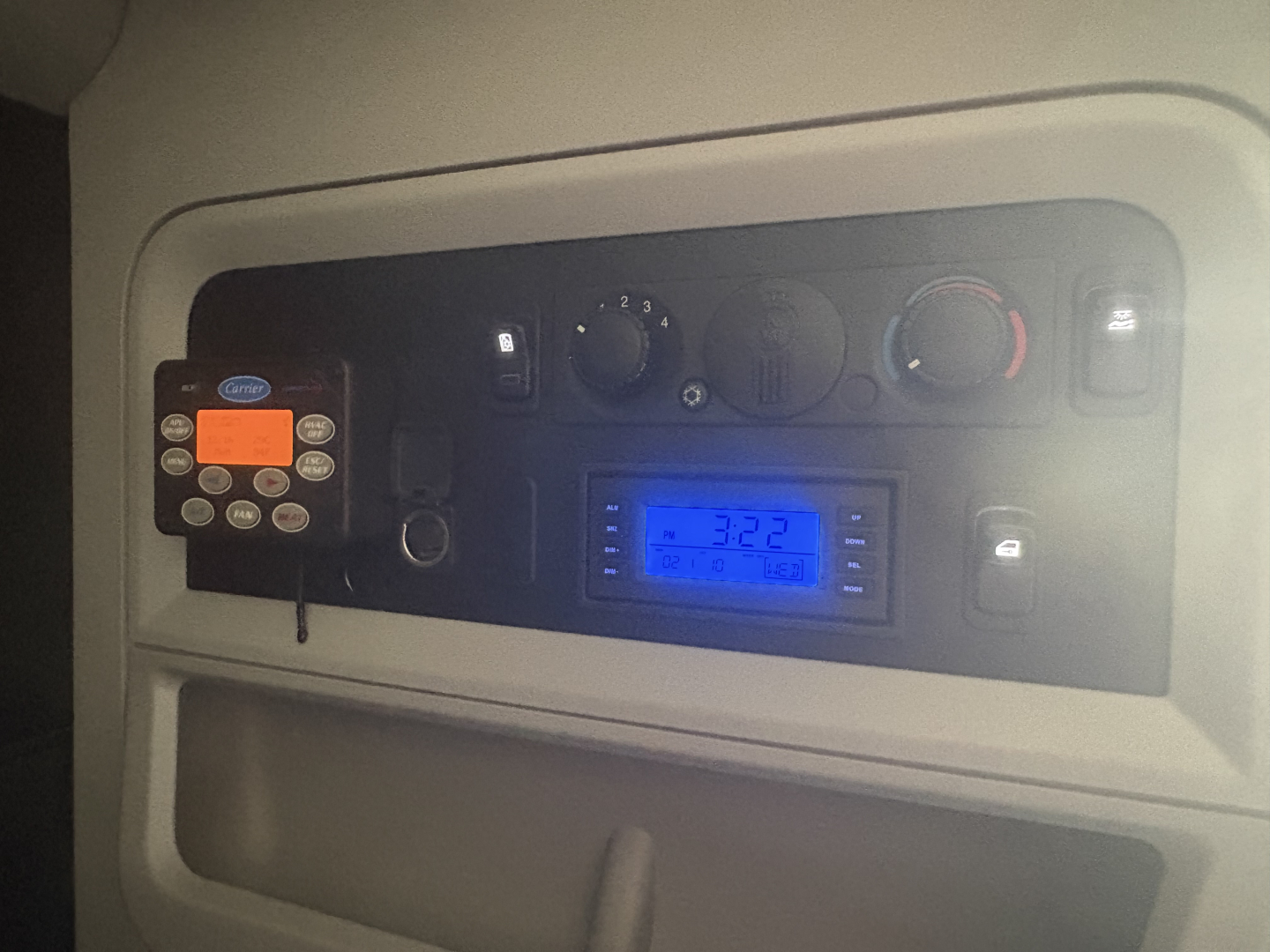 Kenworth T680 dash panel with control knobs and a blue digital display showing numerical values, and a small remote/bracket device mounted on the left.