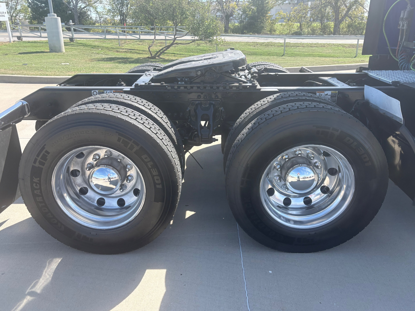 Dual rear axles of a Kenworth truck chassis with shiny chrome wheels and mounted tires.