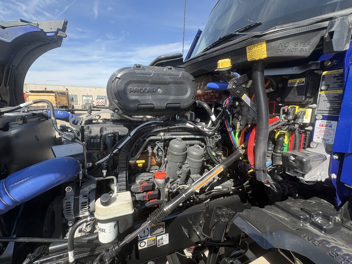 Kenworth T680 engine bay with 6.0-liter V8? engine cover labeled 'WORQU??' visible air intake, wiring, hoses, and accessory components in front compartment.