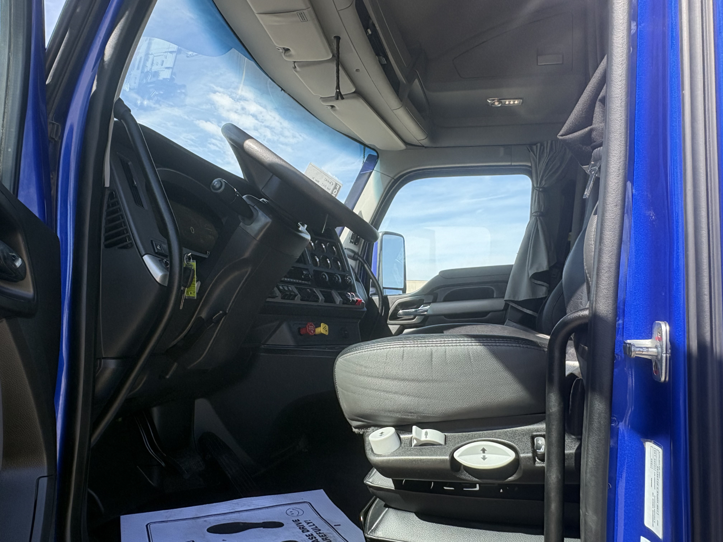 Kenworth T680 cab interior view from driver’s door showing steering wheel, seats, dashboard, and sun visor; blue exterior visible.