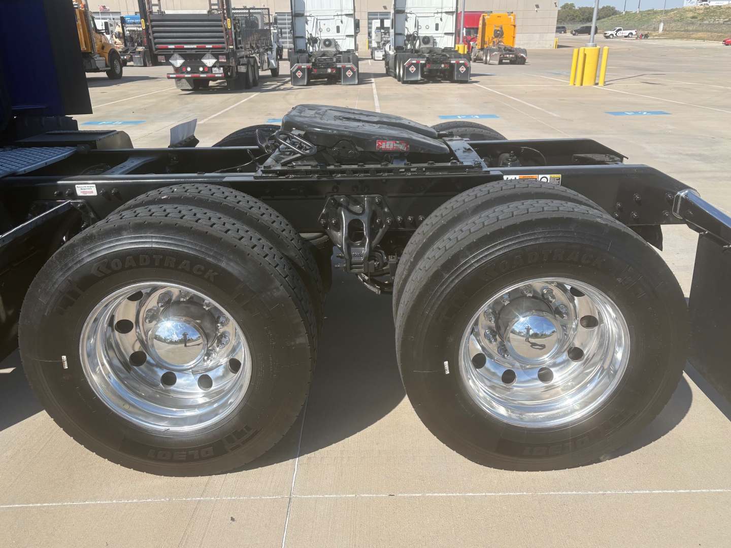 Kenworth T680 rear wheel assembly showing dual rear tires and suspension undercarriage in a parking lot.