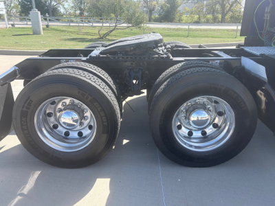 Dual rear axles of a Kenworth truck chassis with shiny chrome wheels and mounted tires.
