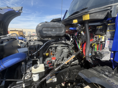 Kenworth T680 engine bay with 6.0-liter V8? engine cover labeled 'WORQU??' visible air intake, wiring, hoses, and accessory components in front compartment.