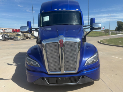 Kenworth T680 front view showing blue cab, chrome grille, and large side mirrors. Grille has Kenworth emblem; headlights visible; bumper area with lower grille.