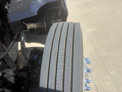 Kenworth T680 front wheel and front axle area with vertical treaded tires and surrounding engine bay components.