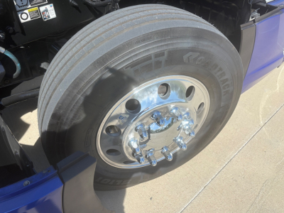 Kenworth T680 front wheel close-up showing chrome multi-hole hub with lug nuts and tire treads.