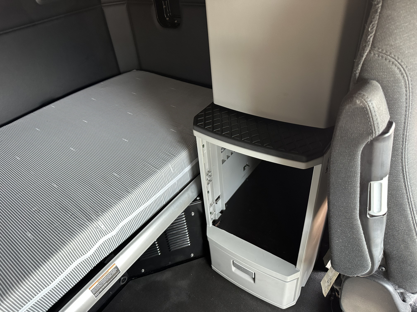Kenworth T680 cab interior showing sleeper area with mattress, storage cabinet, and center console shelf.