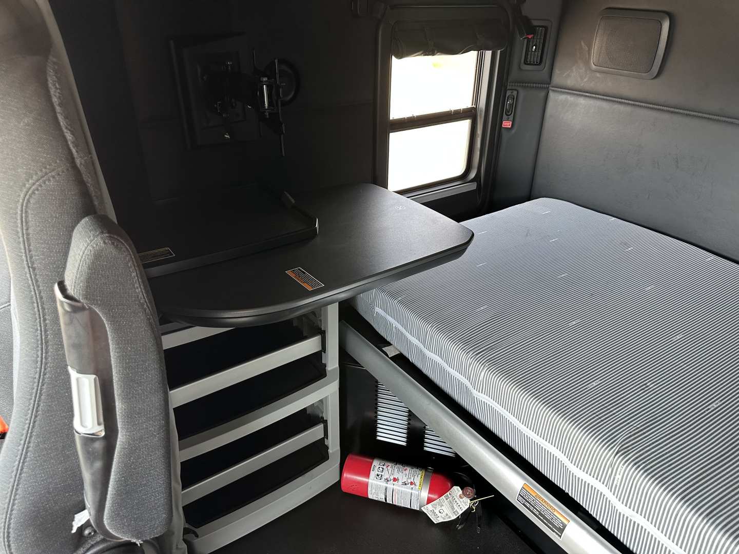 Kenworth T680 cabin interior showing sleeper bed and storage cabinet with table, 2023 model year.