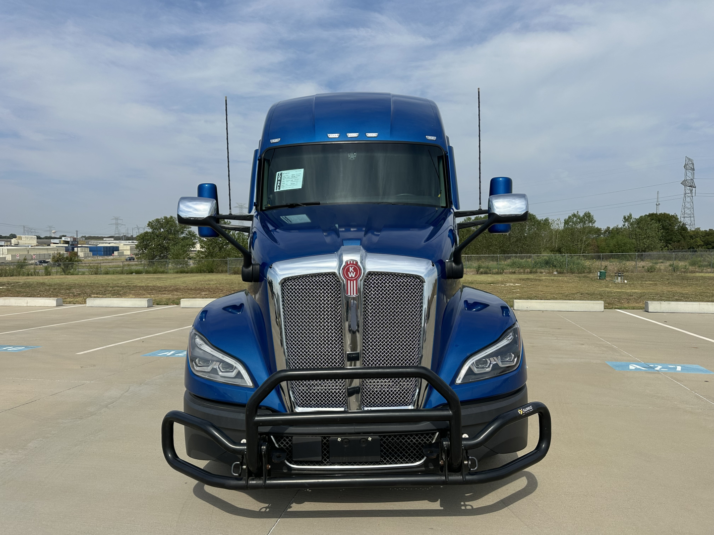 Kenworth T680 front view in blue with grille guard and bumper, cab mirrors, and daytime running lights visible.