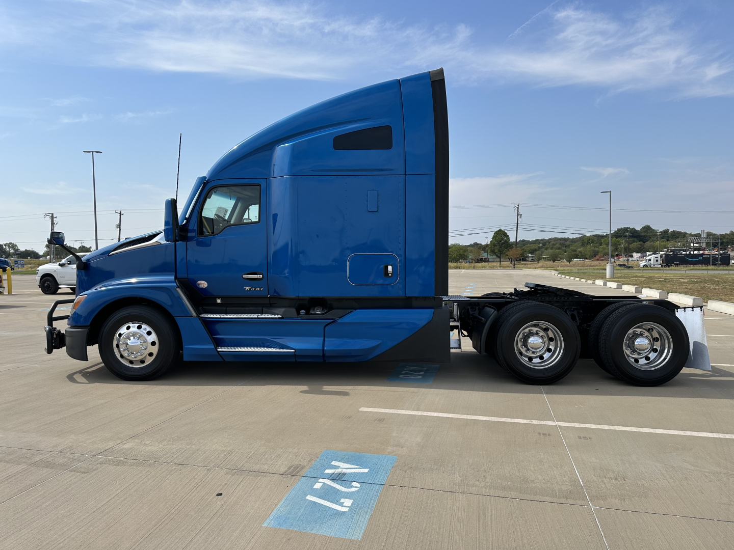 Blue 2023 Kenworth T680 tractor cab side profile showing sleeper cab, six rear wheels, fuel tanks, and step. Visible text includes VIN and stock numbers in listing context.