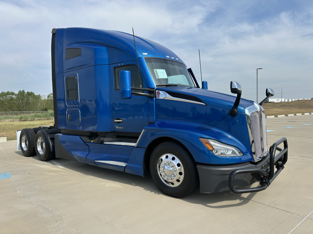 Kenworth T680 blue semi-truck in a parking lot, side view showing front grille guard and sleeper cab