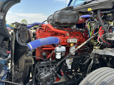 Truck engine bay showing red Cummins X15 engine with blue intake hose and various wiring harnesses.