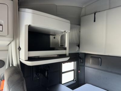 Kenworth T680 sleeper cab interior showing a mounted refrigerator/freezer compartment and storage cabinet with a window and seating area.