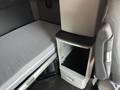 Kenworth T680 sleeper cab interior showing storage compartment and passenger seat with open under-dash area.