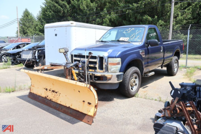 Blue 2008 Ford F-350 Super Duty pickup with a large rusted snow plow blade attached in the front, extended cab, in a lot with other equipment.