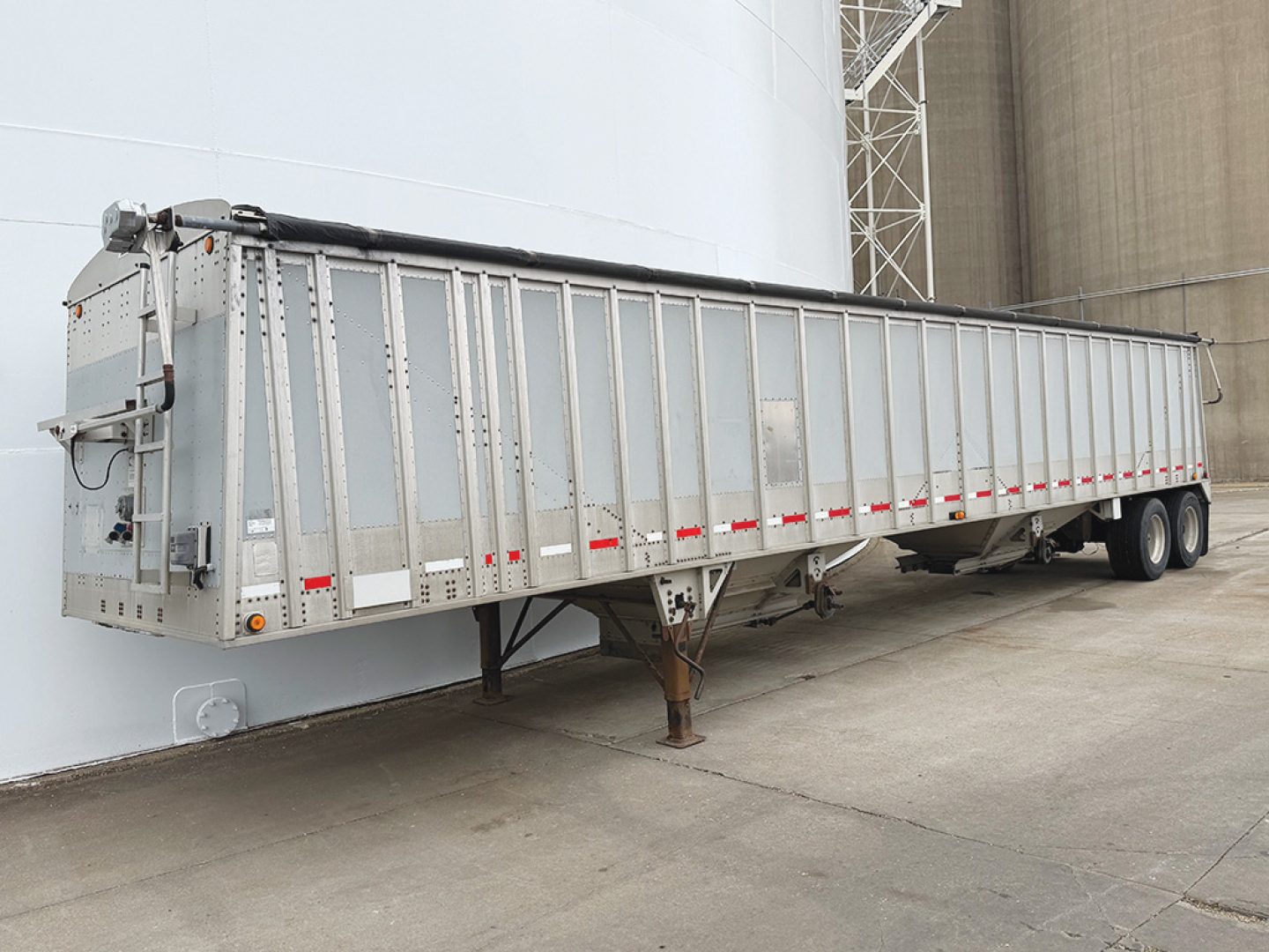 2009 aluminum hopper bottom grain trailer in-service view showing side panels, underside hitch, landing gear, and dual axles.