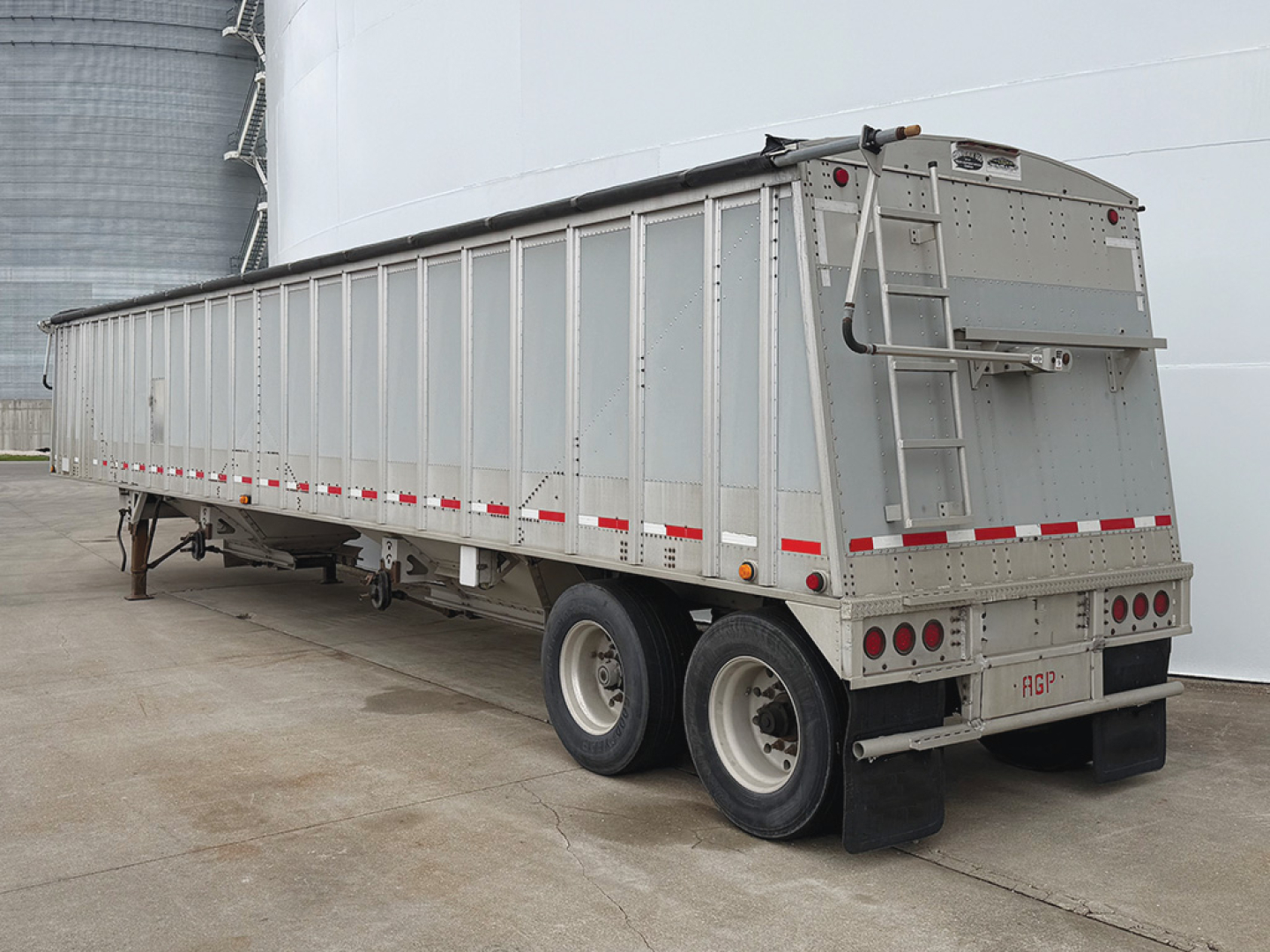 Trailer: aluminum hopper bottom grain trailer, rear and side view showing dual rear axles, ladder, and reflective striping.