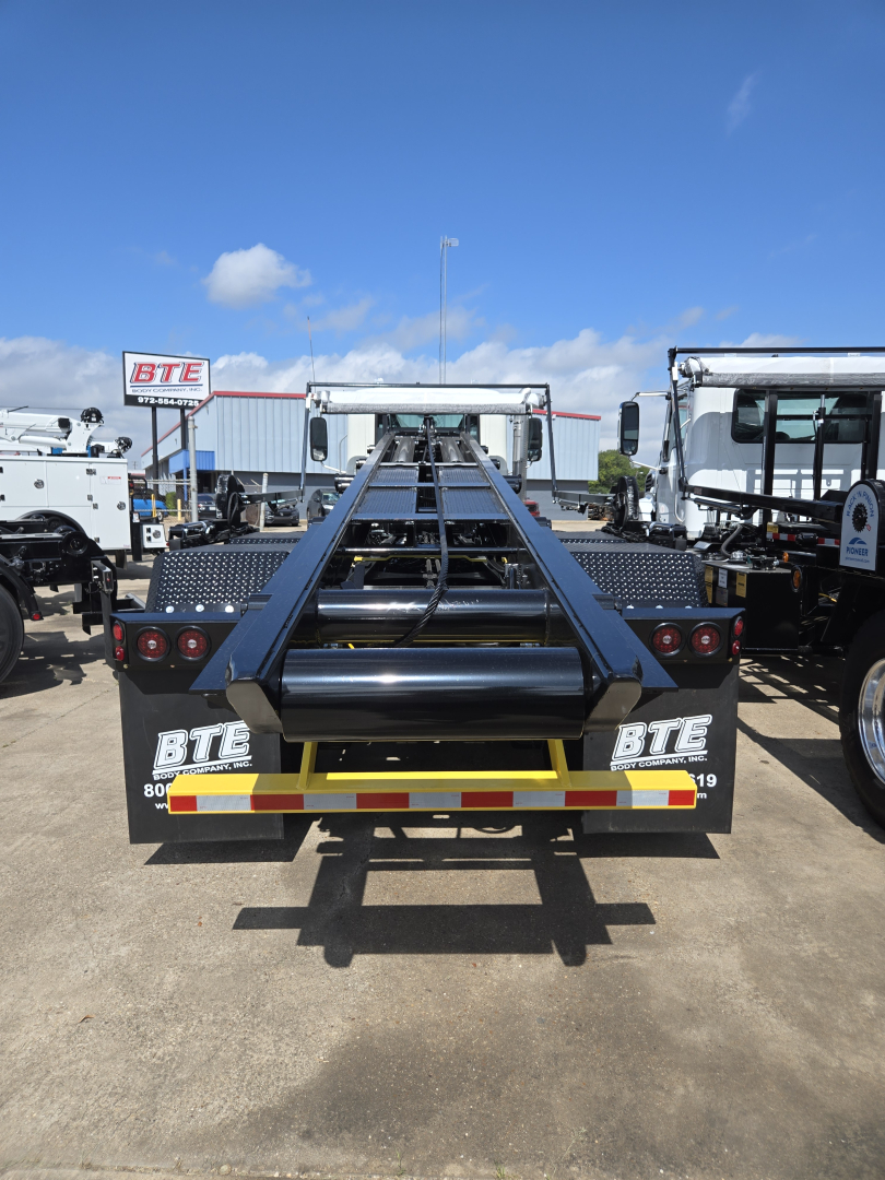 Rolloff truck rear showing BTE branding and reflective strip, with a hydraulic hooklift frame and bumper lights.